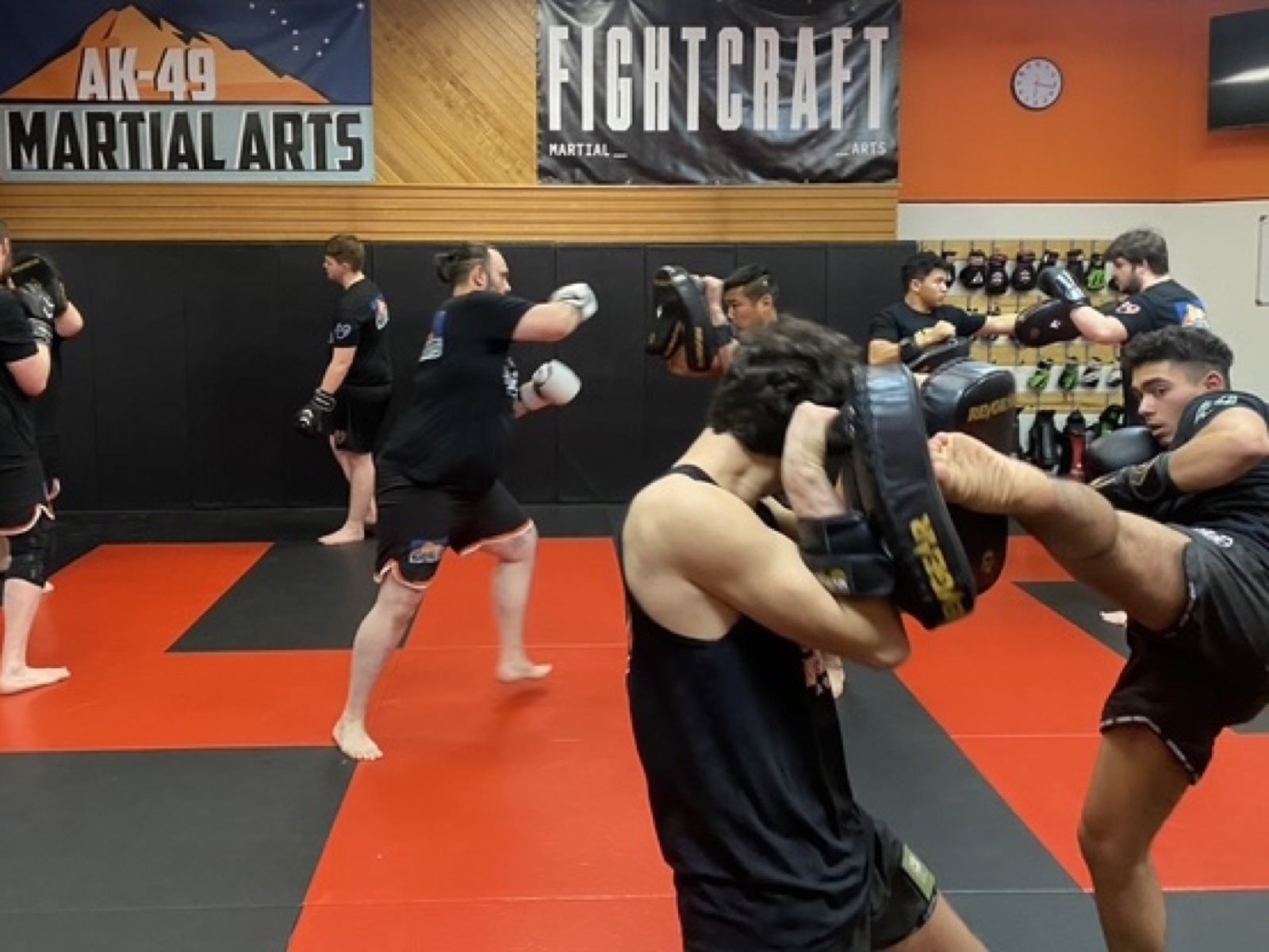 A student kicks pads held by a training partner under the AK-49 Martial Arts banner