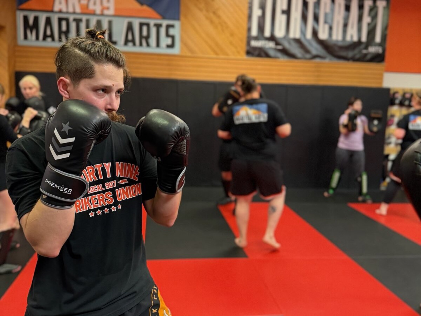 An adult student in boxing gloves during a kickboxing class under the AK-49 Martial Arts banner